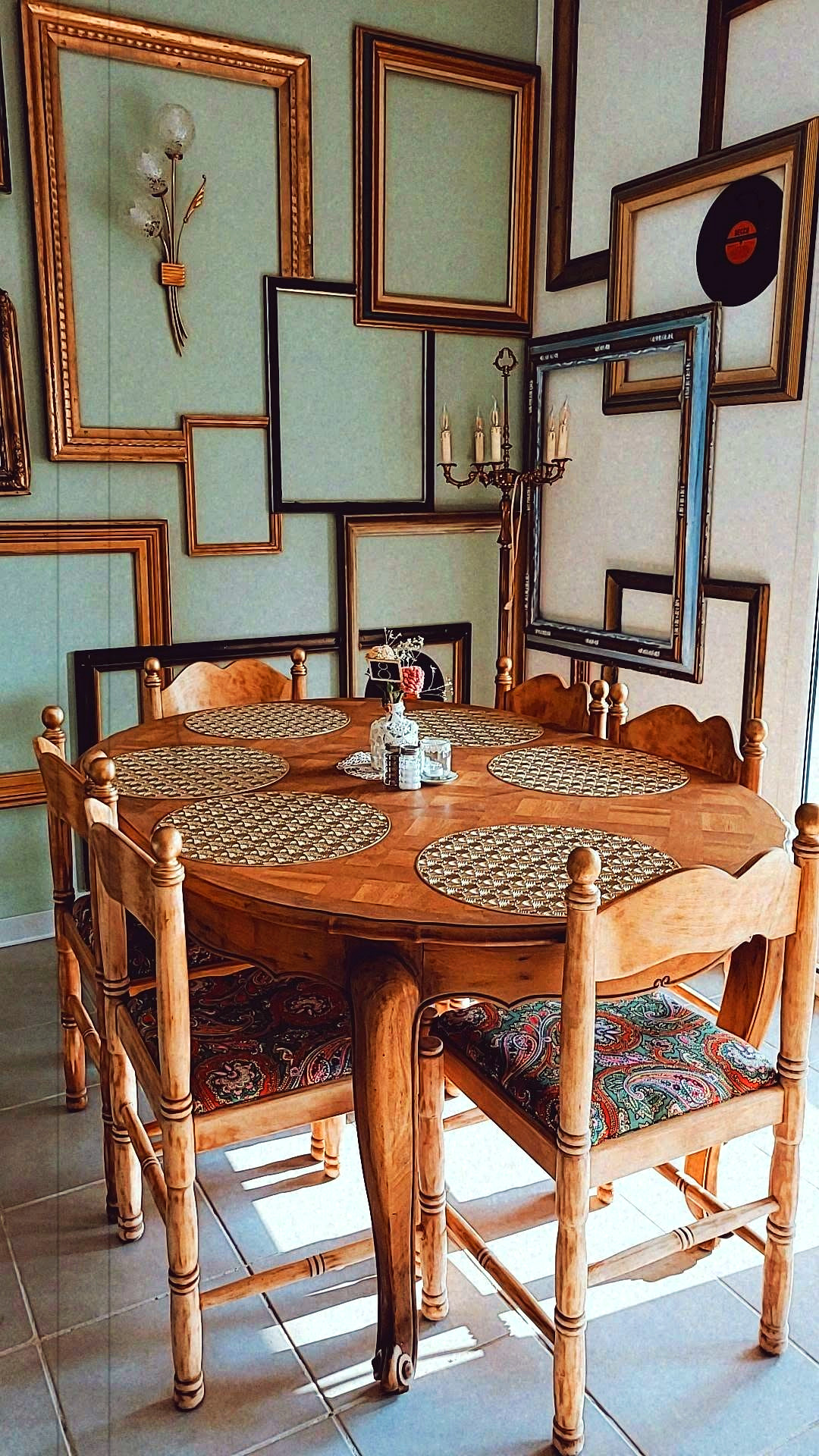 Le mur de cadres dorés de la salle, chinés un à un, et la grande table ronde en bois