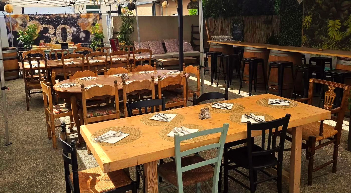 La terrasse couverte dressée pour le service, tables en bois et chaises