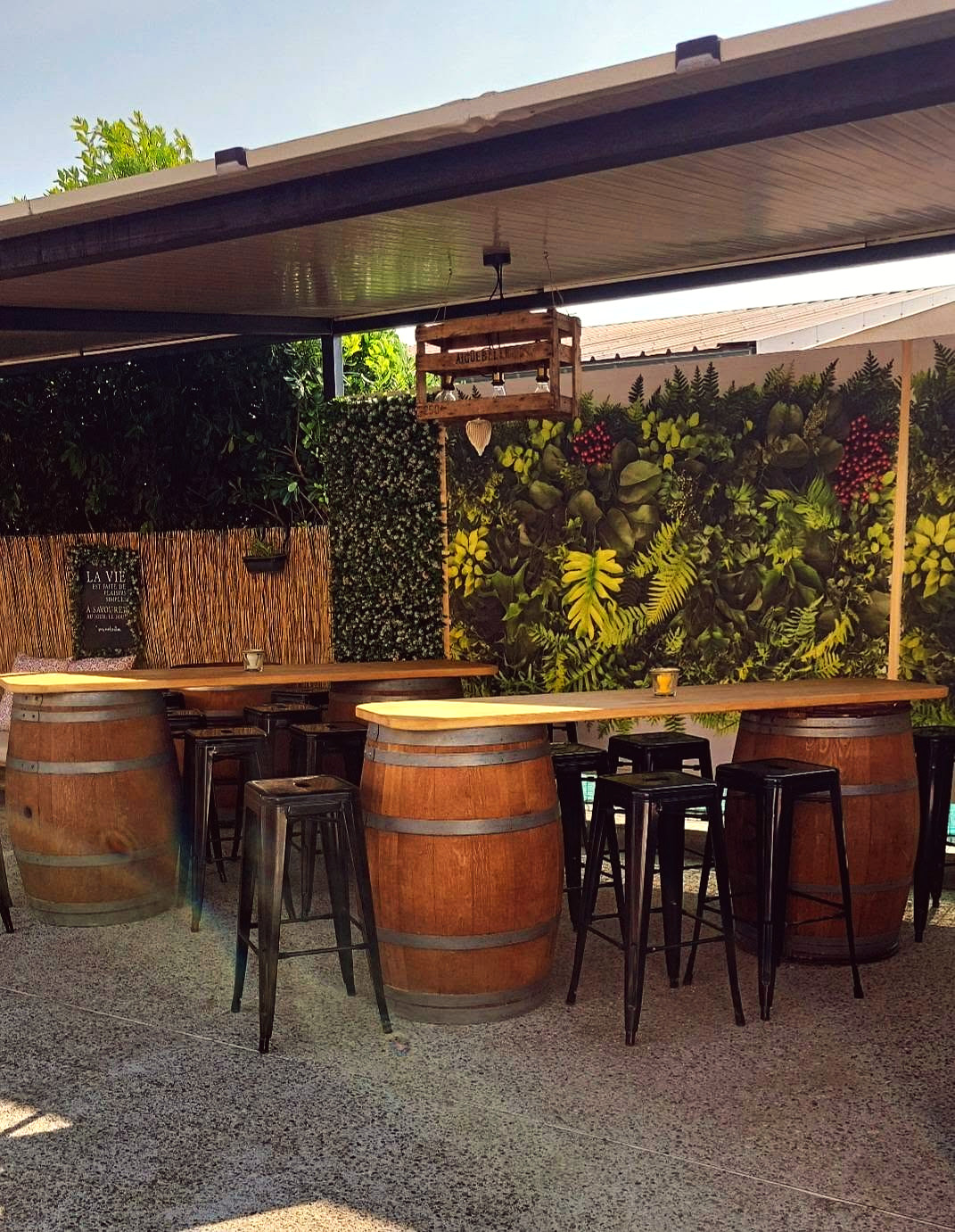 La terrasse couverte : tonneaux en guise de tables hautes, tabourets noirs, mur végétal
